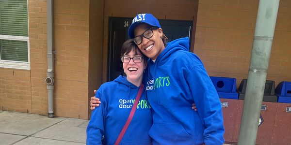 Two people in blue hoodies smiling and hugging outside a building.