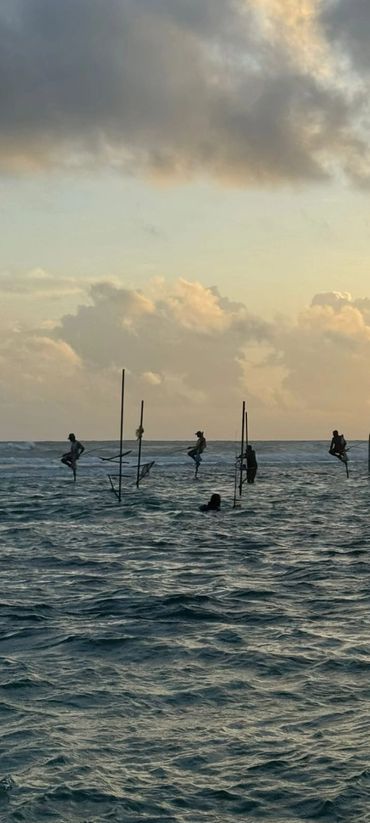 Fishermen perched on stilts above the ocean at sunset.