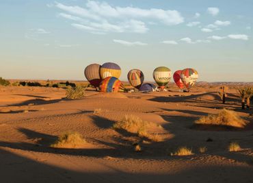 Hot air balloons resting on a desert landscape at sunset.