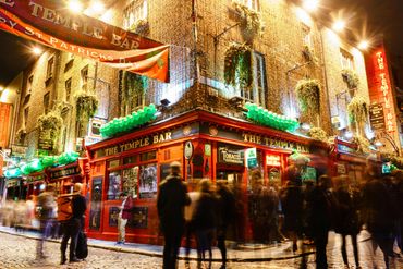 The lively Temple Bar pub illuminated with green lights and bustling with people at night.