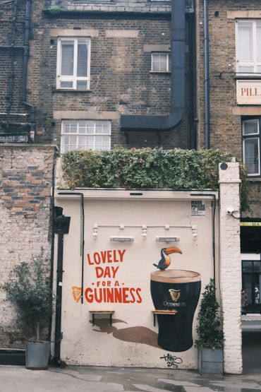 Mural of a Guinness pint and toucan with 'Lovely Day for a Guinness' text on a brick wall.