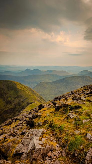 Rocky mountain ridge with layers of distant hills under a cloudy sky.