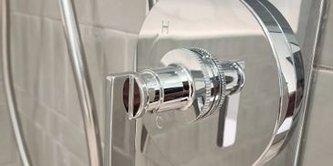 Close-up of a shiny chrome shower control handle on a tiled wall.