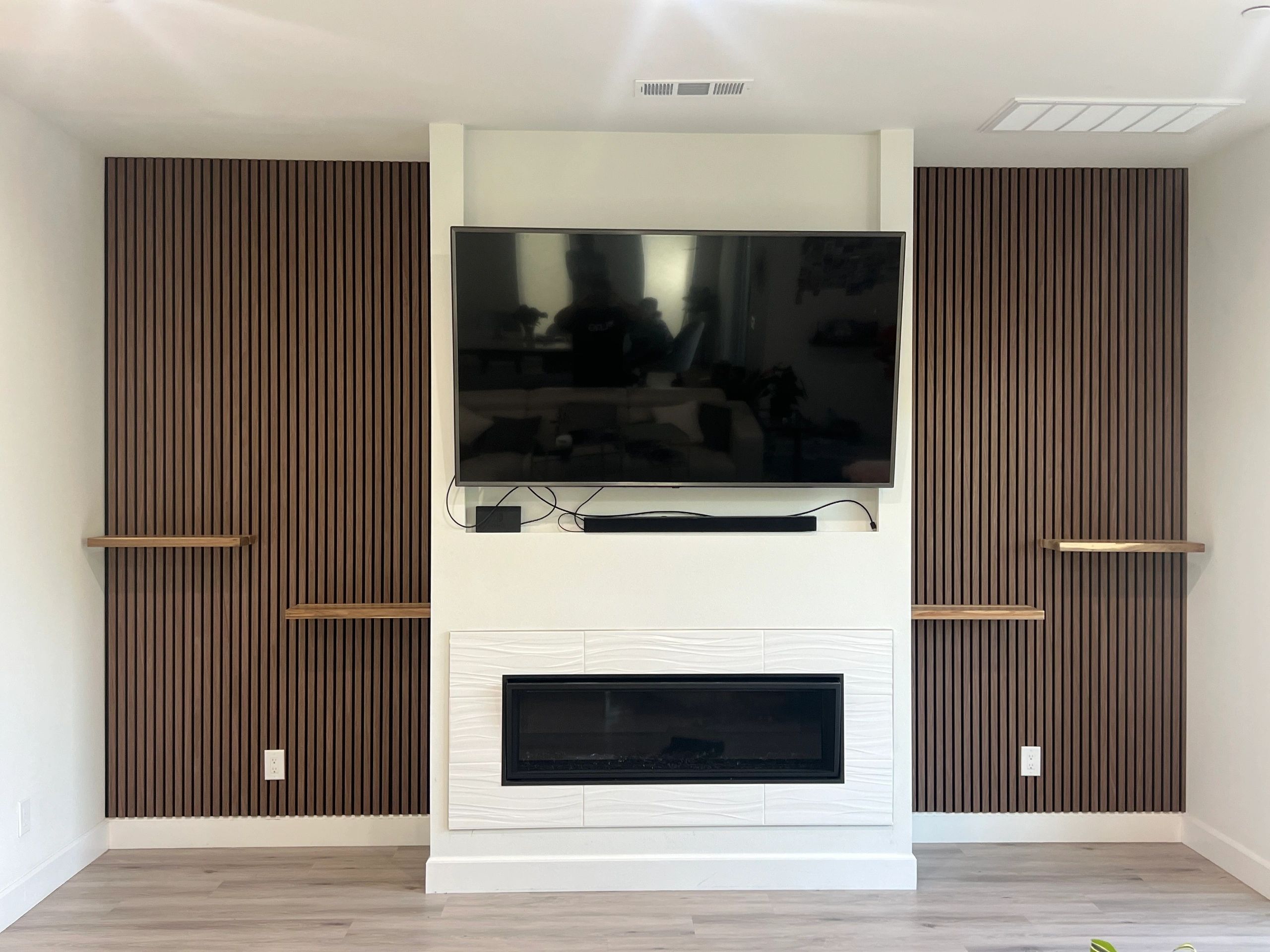 Modern living room with a mounted TV, fireplace, and wooden slat wall panels.