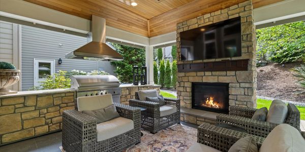 Cozy outdoor patio with stone fireplace, TV, and wicker seating.