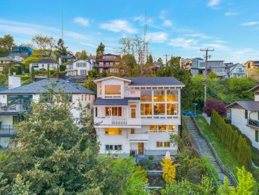 Large modern white house with big windows on a hillside in a residential area.