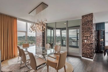 Modern dining room with glass table and elegant chandelier overlooking a scenic view.