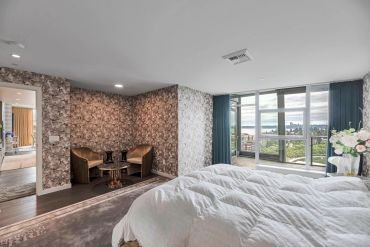 Modern bedroom with floral wallpaper, cozy seating area, and large windows overlooking a cityscape.