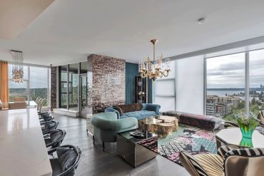 Modern living room with large windows and stylish furniture overlooking a cityscape and water.