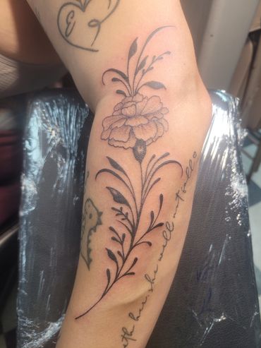 Delicate floral tattoo with cursive script on forearm.