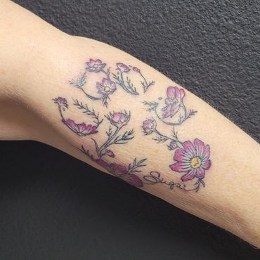 Delicate pink flower tattoo with the word 'Sugar' on a forearm.