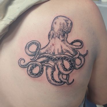 Black ink octopus tattoo on upper back with detailed tentacles.