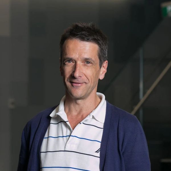 Man smiling wearing a white striped polo and blue cardigan.