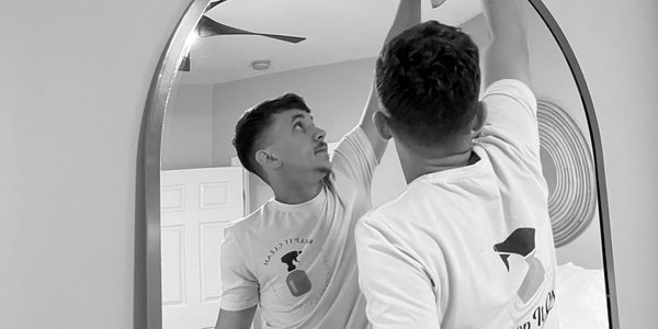 Man cleaning a large round mirror with gloves and a cloth.