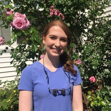 Smiling woman in blue scrub top in a garden with pink roses.