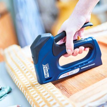 Hand using a blue Rapid stapler on fabric.