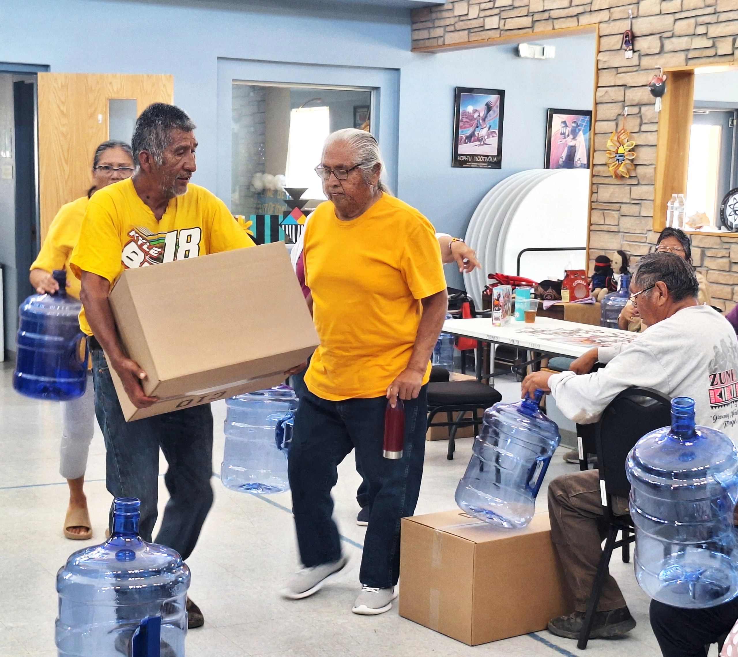 Community members handling boxes and large water jugs indoors.