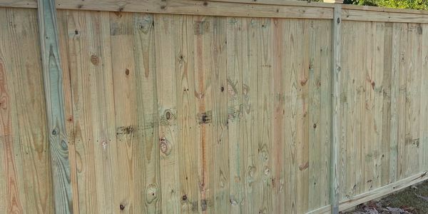 New wooden fence with leaf-covered grass and bare trees under clear blue sky.
