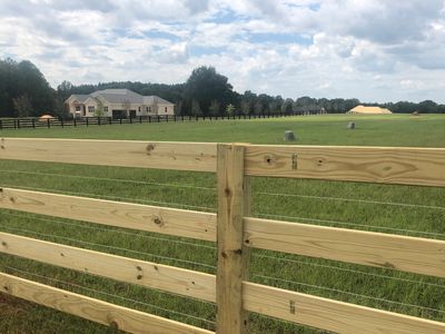 Wooden fence enclosing a grassy field with a house in the background.