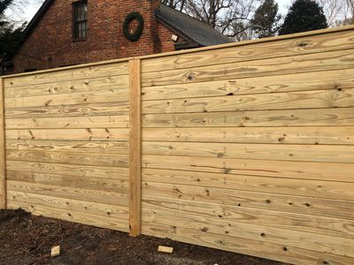 Freshly built wooden fence in front of a brick house with a wreath.