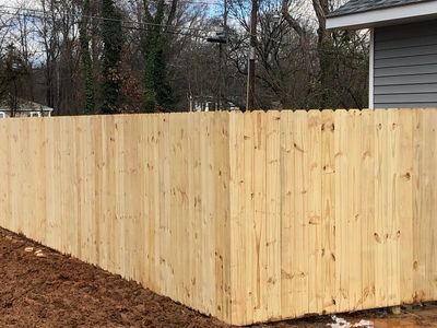 A newly built wooden fence beside a gray house on muddy ground.
