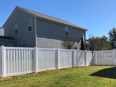 A white vinyl fence enclosing a backyard with green grass under a clear blue sky.