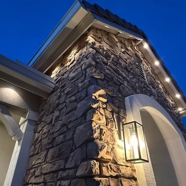 Stone pillar with illuminated lantern and roofline lighting at dusk.