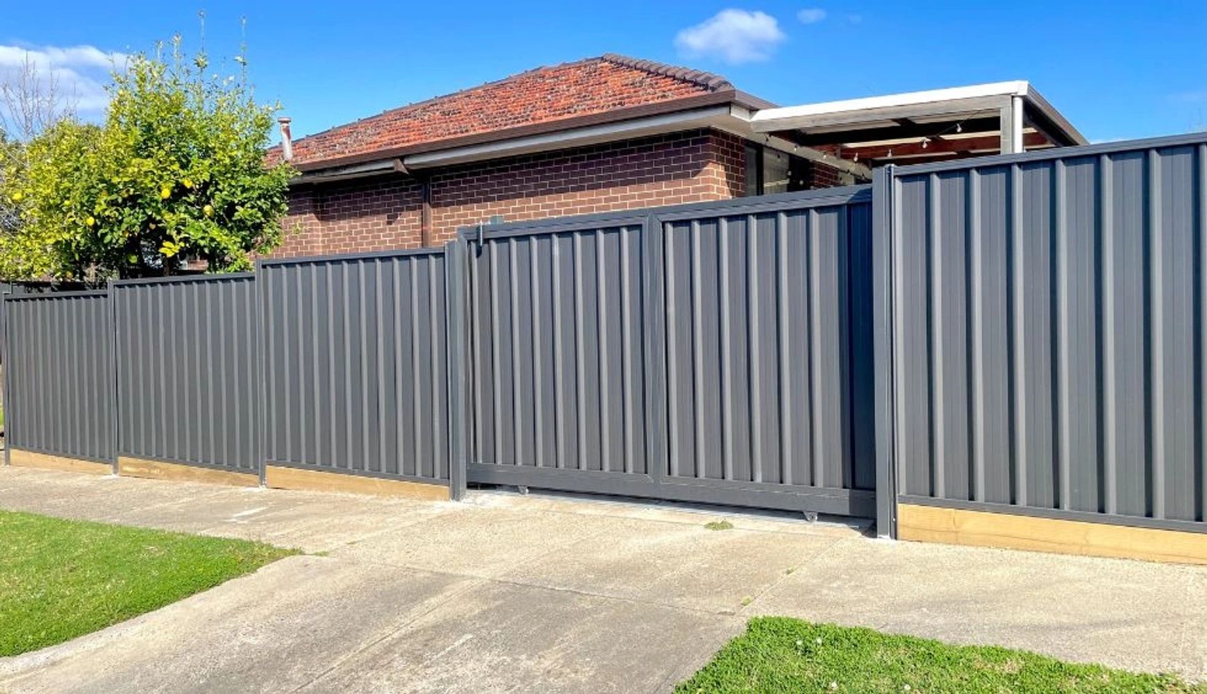 Modern gray metal fence around a suburban brick house on a sunny day.