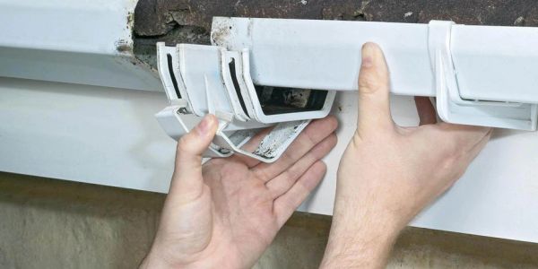Hands repairing a white gutter clip on a roof edge.