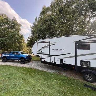 Blue truck towing a white Reflection trailer on a grassy area with trees.