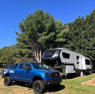Blue pickup truck parked beside a large RV under clear blue skies.