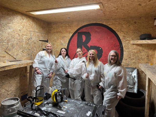 5 woman dressed in boiler suits in the rage room smiling