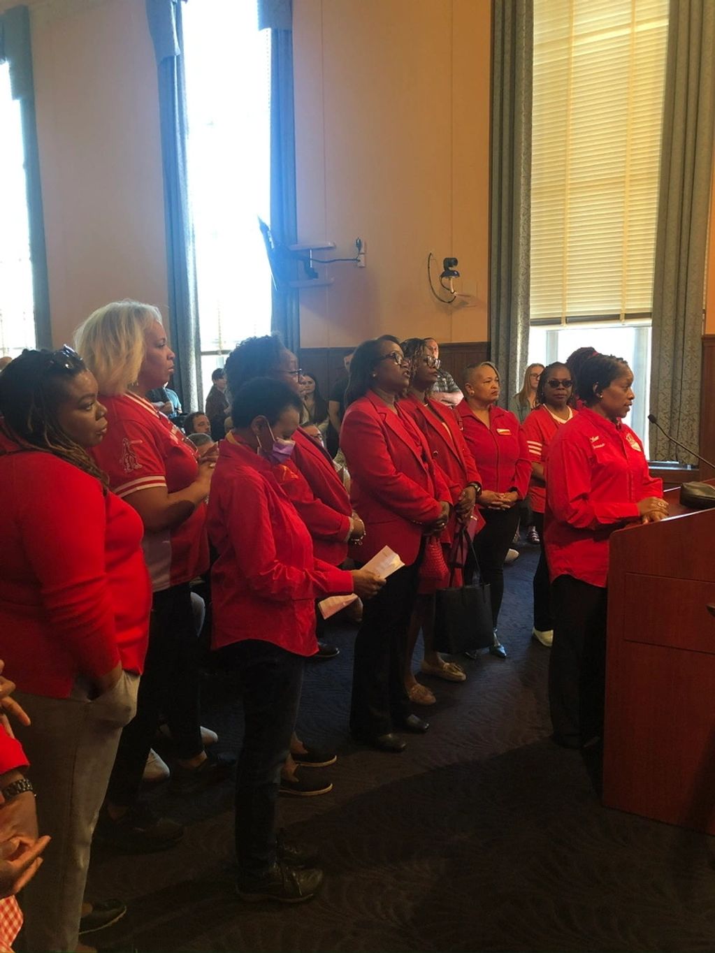 Group of women in red speaking at a podium in a formal setting.