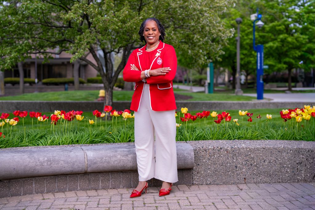 Woman in red blazer and white pants stands confidently in front of colorful tulips.