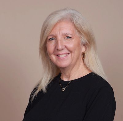 Smiling middle-aged woman with blonde hair in a black top against a beige background.