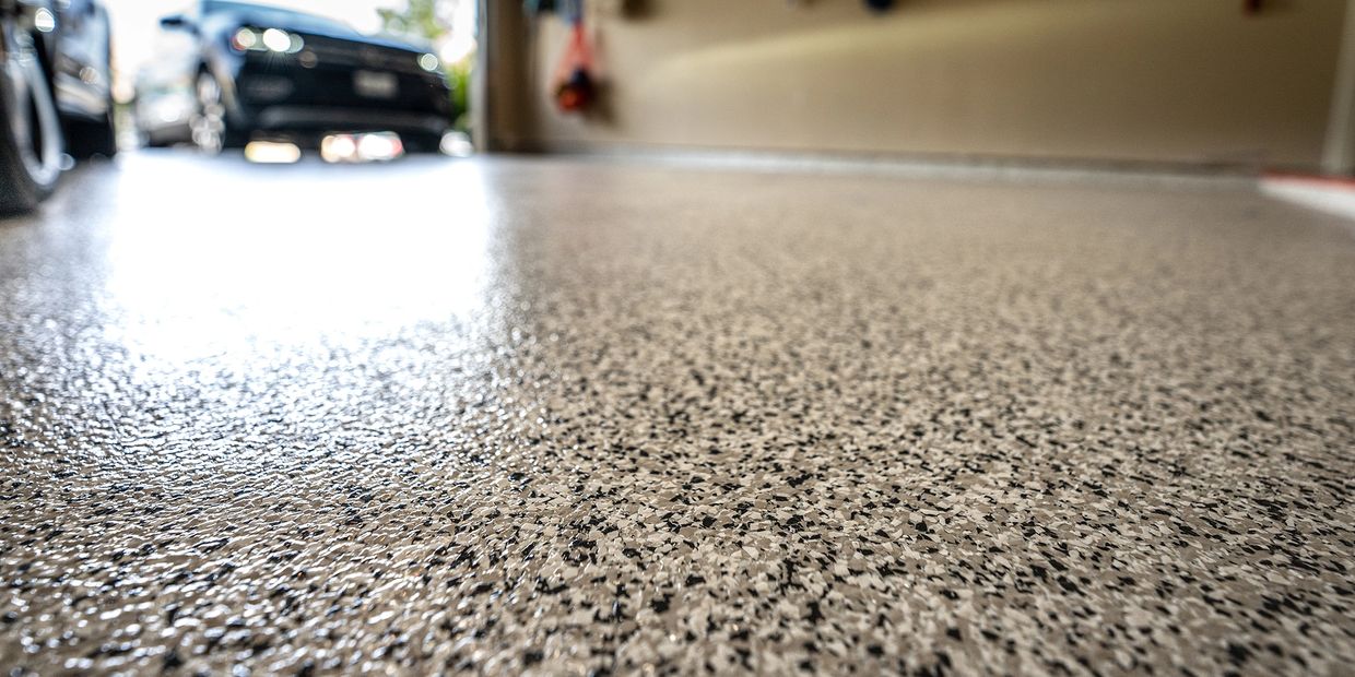 Close-up of a speckled epoxy garage floor with cars in the background.