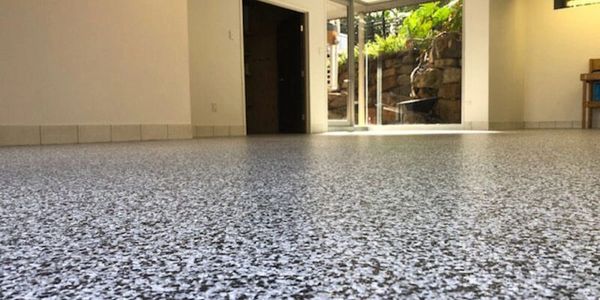 Close-up of a speckled epoxy floor in a bright room with an open door to a garden.