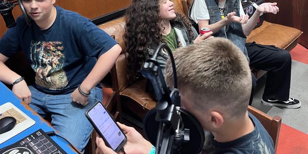 Teenagers hang out in a casual room with a microphone and phone.