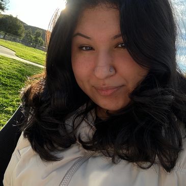 Woman with nose ring smiling outdoors in sunlight.