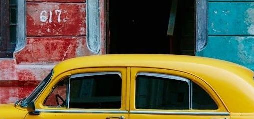 Bright yellow vintage car parked against colorful old buildings.