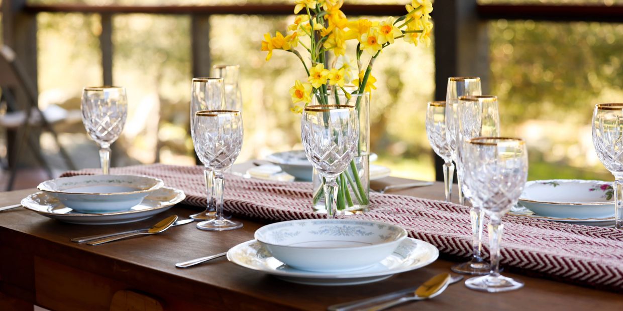 Elegant dining table set with crystal glasses and yellow flowers in natural light.