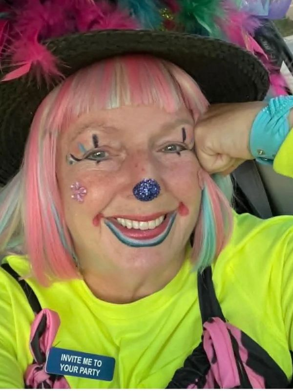 Smiling woman in colorful clown makeup and wig with party invitation badge.