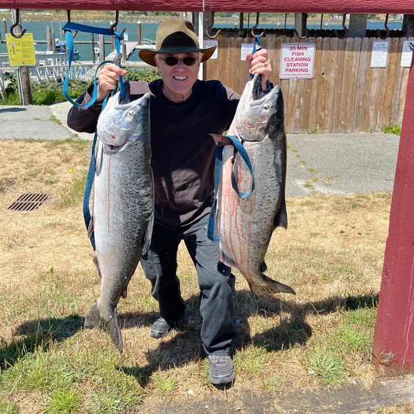 Man proudly holds two large fish caught during a fishing trip.