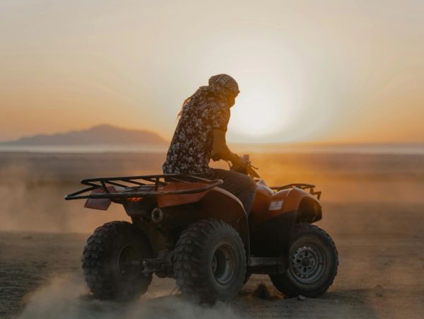 Person riding an ATV at sunset on a dusty terrain.