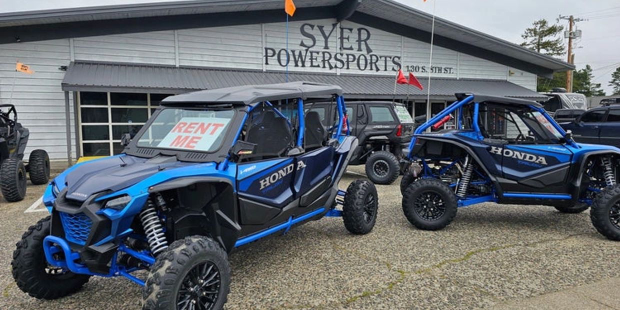 Two blue Honda off-road vehicles parked outside Syer Powersports with a rent sign.
