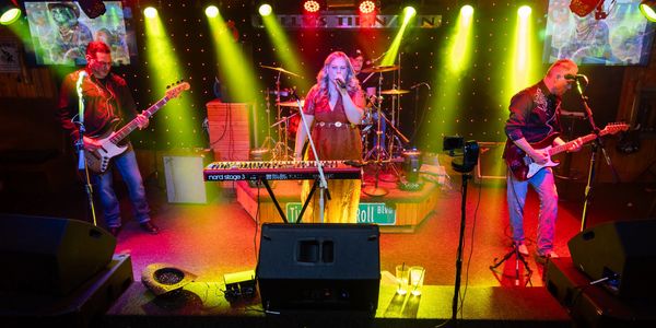 A three-member band performing on stage with colorful lights.