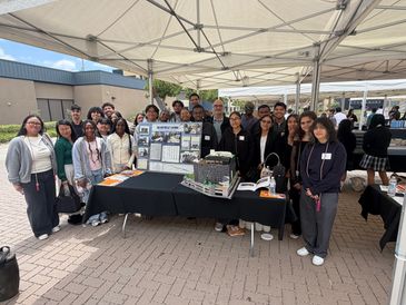 Group of students and teachers presenting a project under a canopy outdoors.