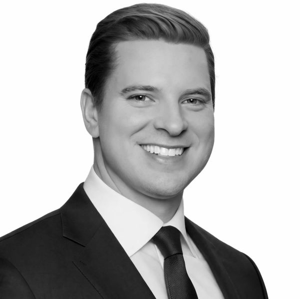 Professional black and white headshot of a smiling man in a suit and tie.