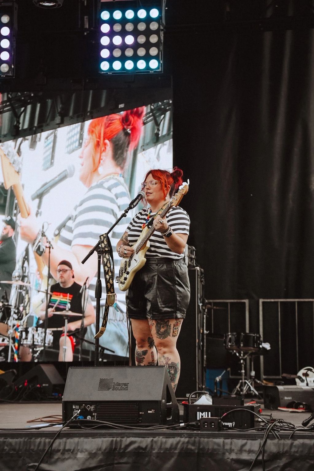 Musician with red hair playing bass guitar on stage.