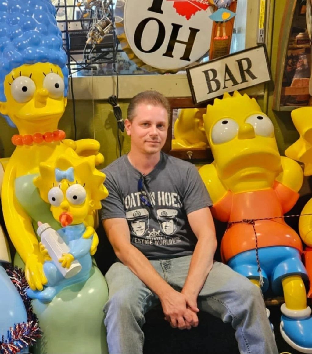 Man posing with Simpsons character statues in a bar.